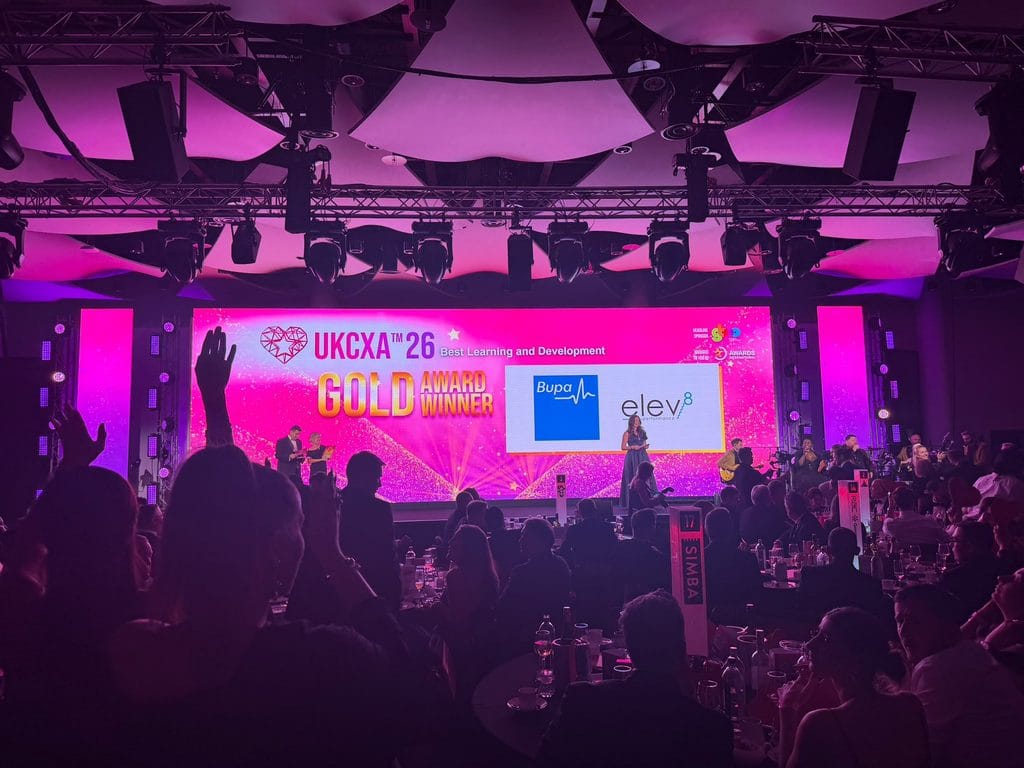 Stage screen at UKCXA 2026 announcing Bupa and Elev-8 as Gold winners for Best Learning and Development